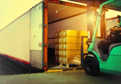 Forklift driver safely loading boxes onto a semi trailer from loading dock, avoiding a work injury.